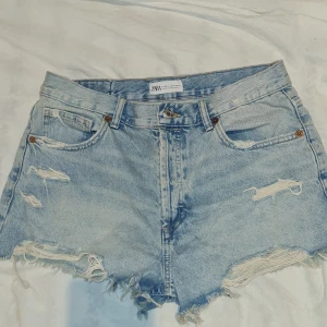Ljusa jeansshorts från Zara - Snygga ljusa jeansshorts från Zara med slitna detaljer och fransig kant. Perfekta för en avslappnad stil. De har en klassisk femficksdesign och knappgylf.