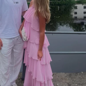 Rosa volangklänning - Charmig rosa långklänning med flera lager av volanger. Klänningen har en ärmlös design och öppen i ryggen! Använd 1 gång! 