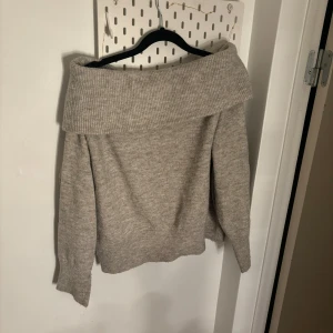 Beige offshoulder stickad tröja - Säljer en mysig beige stickad tröja med offshoulder-design. Tröjan har långa ärmar och en bred ribbad kant vid axlarna som ger en stilren look. Perfekt för kyliga dagar.