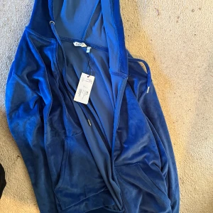 Blå velourjacka med huva - Säljer en mjuk och bekväm blå velourjacka från Bik Bok. Jackan har en dragkedja framtill och en skön huva. Perfekt för en avslappnad stil. 🌀I nytt skick med prislapp. Finns även byxor till (fråga efter bild)