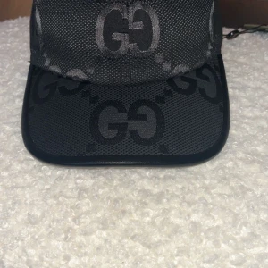 Svart Jumbo gg-keps - Snygg svart keps från Gucci med det ikoniska GG-mönstret. Kepsen har en justerbar rem baktill för perfekt passform. Perfekt för att ge din outfit en lyxig touch.