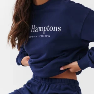 Mörkblå Hamptons tröja - Säljer en mörkblå sweatshirt med texten 'The Hamptons' och koordinater tryckta på framsidan. Tröjan har långa ärmar och en rund halsringning. Perfekt för en avslappnad stil.