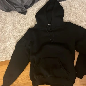 Svart hoodie från BikBok - Säljer en klassisk svart hoodie från BikBok i storlek XS. Den har en praktisk ficka framtill och justerbar huva med snören. Perfekt för en avslappnad stil.