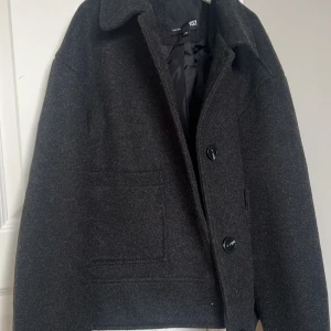 Svart kappa från 157 - Snygg svart kappa från 157 i storlek XS. Jackan har en klassisk design med knappar framtill och två fickor. Perfekt för kyligare dagar.