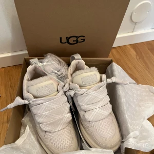 Beige sneakers från UGG - Säljer ett par snygga beige sneakers från UGG med breda snören och fluffig insida. De kommer i originalkartong och är helt oanvända och nya. 