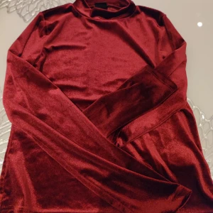 Vinröd polotröja från Gina Tricot - Snygg vinröd polotröja från Gina Tricot i ett glansigt material. Perfekt för att ge en touch av elegans till din outfit. Tröjan har långa ärmar och en klassisk polokrage.