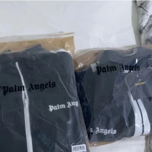 Palm Angels   - Snyggt grått träningsset från Palm Angels med vit dragkedja och vita ränder längs ärmar och ben. Setet har en sportig look med logotypen tryckt på både jacka och byxor. Perfekt för en avslappnad stil passar nästan alltid jätte skönt och ha den kan mötas i Linköping och Norrköping resten funkar med frakt 🫶🏽