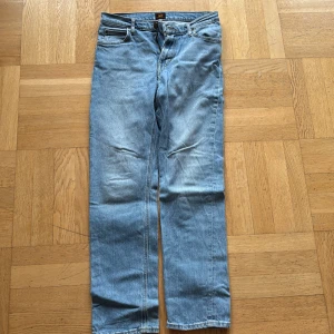 Blå jeans från Lee - Säljer ett par klassiska blå jeans från Lee. De har en straight passform och är tillverkade i denim med en snygg ljusblå tvätt. Byxorna har fem fickor och en dragkedja med knappstängning. Perfekta för en avslappnad stil.