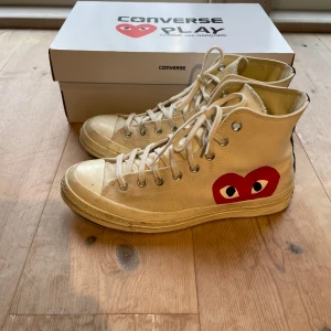 Converse x Comme des Garçons Play sneakers - Säljer ett par Converse x Comme des Garçons Play sneakers i beige med det ikoniska röda hjärtat på sidan. Skorna har snörning och är i hög modell. Perfekta för en stilren look! De är lite smutsiga som syns på bild men inget extremt. Låda medföljer, inköpta för 1300kr. Vid frågor skriv!