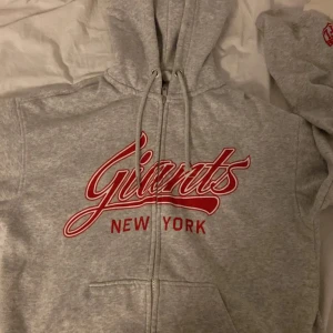 Grå hoodie med Giants New York-tryck - Säljer en grå hoodie med dragkedja och tryck av Giants New York i rött. Är använd få tal gånger och har inga fläckar eller märken.pris kan diskuteras