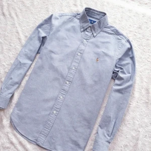 Ralph Lauren - “Hej! Säljer en klassisk Ralph Lauren-skjorta i storlek Medium. Ljusblå med små gråa drag med broderad logotyp. Skjortan är i utmärkt skick, utan tecken på användning. Perfekt för både vardag och fest. Hör av dig vid eventuella frågor!”