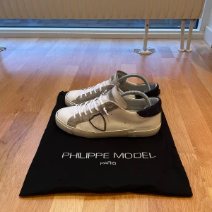 Vita sneakers från Philippe Model - Snygga vita sneakers från Philippe Model med grå och svarta detaljer. Skorna har snörning och en stilren design som passar perfekt till vardags. De är tillverkade i skinn och har en bekväm passform. Stora i storlek, passform 42. Nya snören på! Okej skick! Obs: Dustbag ingår! Hör av er vid fler bilder och frågor! MVH Ludvig 