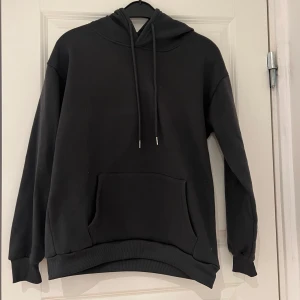 Grå hoodie med ficka - Säljer en grå hoodie med känguruficka och justerbar huva. Perfekt för en avslappnad look. Den har långa ärmar och ribbade muddar vid ärmslut och nederkant. Sliten.