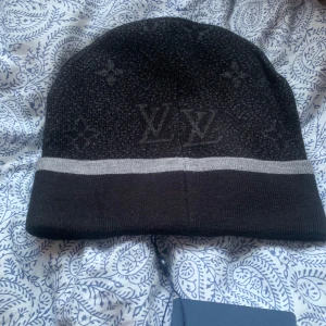Svart mössa - Snygg svart mössa  med grå rand och diskret mönster. Broderad logotyp framtill ger en exklusiv touch. Perfekt för att hålla stilen i kallare väder. Priset går självklart att diskutera😁