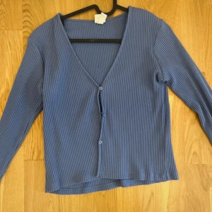 Blå ribbad kofta - Säljer en blå ribbad kofta med v-ringning och knappar framtill. Perfekt för lager-på-lager och passar till många olika stilar. Ett mångsidigt plagg för garderoben!