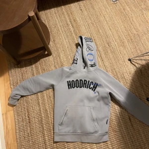 Grå hoodie från Hoodrich - Säljer en snygg grå hoodie från Hoodrich i storlek S. Den har en stor svart logga på bröstet och coola detaljer på luvan. Perfekt för en avslappnad stil och passar bra till både vardag och chill. Grymt skön och i bra skick!