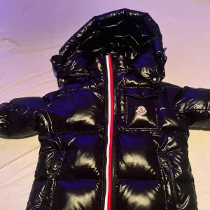 Moncler jacka  - Säljer en snygg Moncler jacka i mycket bra skick. Jackan har en glansig finish och en praktisk huva. Den är långärmad och har en dragkedja framtill med Monclers ikoniska logga på bröstet. Perfekt för kalla vinterdagar! Jag säljer den här jackan på grund av att har ingen användning till den jackan är helt ny 