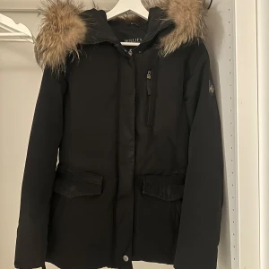 Svart vinterjacka från Hollies - Säljer en snygg svart vinterjacka från Hollies med pälskantad huva. Jackan har långa ärmar och praktiska fickor framtill. Perfekt för kalla vinterdagar! 🖤
