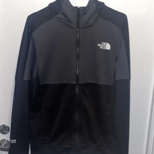 Svart och grå jacka från The North Face - Säljer en svart och grå jacka från The North Face med dragkedja och huva. Jackan har The North Face-logga på bröstet och ärmen. 