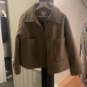Beige kappa  - Säljer en snygg beige kappa från Arket i mycket bra skick. Den har en klassisk design med stora knappar och två praktiska fickor framtill. Perfekt för höst och vår, och ger en stilren look till vilken outfit som helst. Storleken är dam S