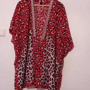Röd leopardmönstrad kaftan - Säljer en supercool röd kaftan med leopardmönster. Den har en djup v-ringning med snygga detaljer längs kanten. Perfekt för en avslappnad dag eller en sommarfest. Passar de flesta storlekar tack vare sin lösa passform.