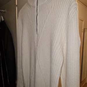 Moncler tröja 1/2 zip - Säljer en snygg vit ribbad tröja från Moncler. Den har en halv dragkedja framtill och ett broderat Moncler-märke på ärmen. Perfekt för kyliga dagar och ger en stilren look. Passar både till vardags och lite finare tillfällen.