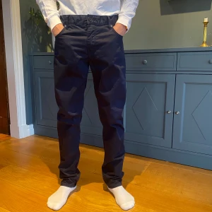 Marinblå byxor från J.Lindeberg - Snygga svarta byxor från J.Lindeberg i en klassisk straight passform. Perfekta för en stilren look med midwaist design och knappar i midjan. 