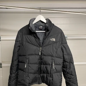 Svart dunjacka från The North Face - Säljer en svart dunjacka från The North Face i bra skick. Jackan har en dragkedja framtill och två praktiska fickor med dragkedjor. Perfekt för kalla vinterdagar med sin varma och quiltade design. Passar både till vardags och utomhusaktiviteter. 🖤Säljes i befintligt skick. Storlek: L/M kids