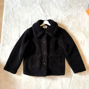 Svart teddyjacka från NA-KD - Mysig svart teddyjacka från NA-KD med stora knappar och två öppna fickor fram. 