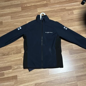 mörk blå jacka från Sail Racing - Snygg mörk blå jacka från Sail Racing med dragkedja och logotypdetaljer på ärmarna. Perfekt för hösten o våren med sin stilrena design och funktionella passform.