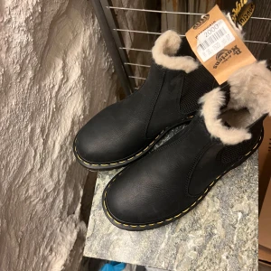 Svarta boots från Dr. Martens med foder - Snygga svarta boots från Dr. Martens med mjukt foder för extra värme. De har en robust sula med bra grepp och klassisk gul söm. Perfekta för kyligare dagar. Helt oanvända. Nypris 2000kr, säljer för 800kr.