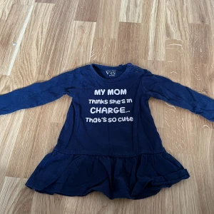 Mörkblå klänning från VRS Fashion - Söt mörkblå klänning från VRS Fashion med texten 'My mom thinks she's in charge... That's so cute' i vitt. Klänningen har långa ärmar och en volangdetalj vid nederkanten.