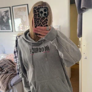 Grå hoodie med tryck - Säljer en grå hoodie med tryck på framsidan. Den har en stor ficka framtill och justerbar huva med snören. Perfekt för en avslappnad stil.