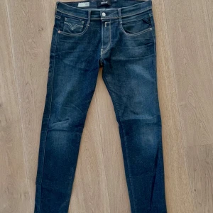 Mörkblå jeans från Replay - Snygga mörkblå jeans från Replay med klassisk femficksdesign och diskret broderi på bakfickorna. Jeansen har en slim passform och är perfekta för en stilren look. Modellen heter Replay Anbass