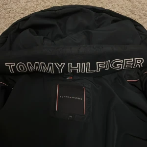 Svart pufferjacka från Tommy Hilfiger - Säljer en svart pufferjacka från Tommy Hilfiger i storlek S. Jackan har en dragkedja framtill och en mysig huva. Perfekt för kalla höst- och vinterdagar. Den är i mycket bra skick och redo för nya äventyr! Skulle rekommendera för 11-12 åringar!