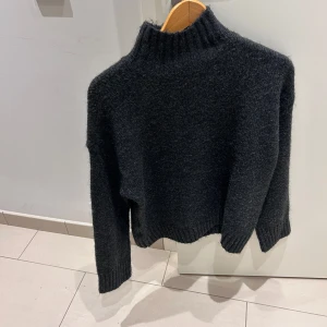 Mörkgrå stickad tröja från Vero Moda - Säljer en mysig mörkgrå stickad tröja från Vero Moda. Perfekt för kyliga dagar med sin höga krage och långa ärmar. Tröjan har en enkel och stilren design som passar till det mesta. Perfekt för både vardag och mysiga hemmakvällar.