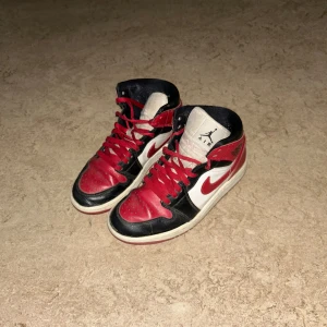 Jordan 1 skor - Säljer ett par klassiska Nike Air Jordans i rött, svart och vitt. Skorna har en snygg design med snörning och den ikoniska Nike-loggan på sidan. Perfekta för både vardag och fest! De är i bra skick med lite slitage på sulan.