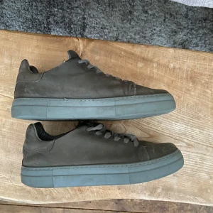 Grön/grå Mocka sneakers  - Säljer ett par grå/gröna sneakers i mocka. Skorna är i bra skicka men mockan har blivit lite sliten och är rätt platt nu. Stilrena passar till allt