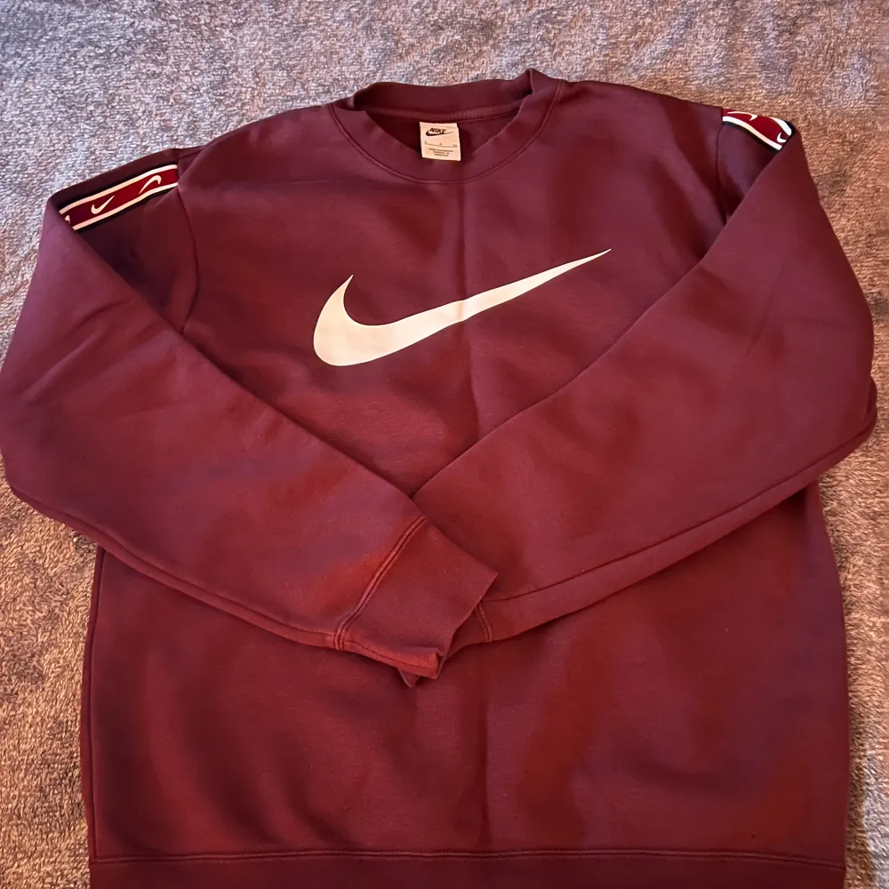 Säljer en snygg vinröd sweatshirt från Nike med det klassiska swoosh-loggan i vitt på bröstet. Tröjan är i bra skick och perfekt för både höst och vinter. Den har långa ärmar och är superbekväm att ha på sig. Perfekt för en casual look eller träning!. Tröjor & Koftor.