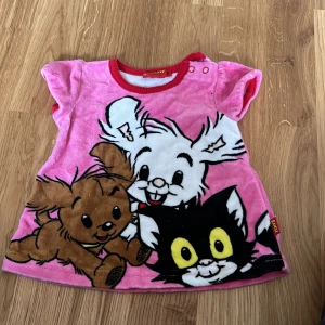 Rosa Bamse-tröja från Lindex - Söt rosa tröja från Lindex med Bamse-motiv. Tröjan har korta ärmar och knappar vid halsen för enkel påklädning. Perfekt för små Bamse-fans!