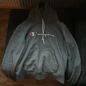 Säljer en grå hoodie från Champion i bra skick. Den har en klassisk Champion-logga på bröstet och en stor ficka framtill. Perfekt för höst och vinter, och den är superbekväm med sin mjuka insida. Passar både till vardags och chillkvällar. 🩶