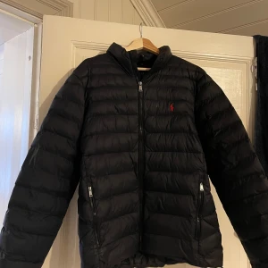 Svart dunjacka Ralph Lauren - Säljer en snygg svart dunjacka från Ralph Lauren i storlek L. Det är en tunnare dunjacka så passar perfekt för vår och höst men funkar även på vintern. Jackan är i fint skick och äkta såklart, inga hål eller defekter. 
