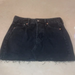 Svart jeanskjol från H&M &Denim - Snygg svart jeanskjol från H&M &Denim i kort modell. Kjolen har en rå kant nertill Perfekt för en avslappnad stil.