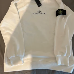  Stone Island sweatshirt  - Snygg vit sweatshirt från Stone Island med deras ikoniska logga på bröstet och en stor logga på ryggen. Tröjan har långa ärmar och ribbade muddar vid ärmslut och nederkant. Perfekt för en stilren och avslappnad look. Sälja pga behöver pengar priset går att diskutera