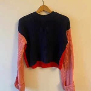 Flerfärgad stickad tröja - Säljer en cool stickad tröja i flerfärgad design. Den har en mörkblå framsida med röd nederkant och en röd baksida. Ärmarna är rosa och ger en härlig kontrast. Perfekt för höst och vår!