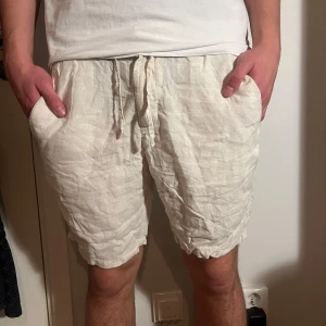 Beige linneshorts med snörning - Säljer ett par bekväma beige shorts i linne med snörning i midjan. Perfekta för sommardagar och avslappnade stunder. De har en normal passform och är i mycket bra skick. Storleken är EUR 46, vilket motsvarar herr M.