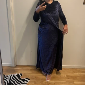 Mörkblå sammet långklänning - Säljer en elegant mörkblå långklänning i sammet. Klänningen har en klassisk design med långa ärmar och en mjuk, glansig yta som ger en lyxig känsla. Perfekt för höst- och vinterfester eller andra speciella tillfällen. Den är i nyskick och redo att bäras av någon som vill känna sig extra glamorös.