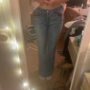 Blå jeans med röda detaljer - Säljer ett par snygga blå jeans med  röda detaljer vid fickorna. De har en klassisk femficksdesign och en bekväm passform. Perfekta för vardagsbruk eller en avslappnad utekväll! Är 171 lång. Kontakta gärna för fler bilder💗 mått rakt över:35cm