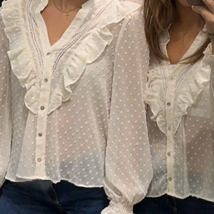 Vit blus med volangdetaljer - Säljer en superfin vit blus med volangdetaljer och prickigt mönster. Blusen har långa ärmar och knappar framtill. Perfekt för både vardag och fest! 💫