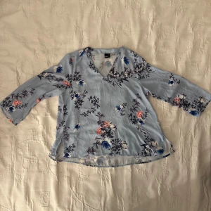 Blommig blus från Gina Tricot - Säljer en superfin blommig blus från Gina Tricot i storlek 36. Den är ljusblå med ett vackert blommönster i blått, vitt och rosa. Blusen har en v-ringad hals och trekvartsärmar, perfekt för varmare dagar. Den är i bra skick och knappt använd!🌸